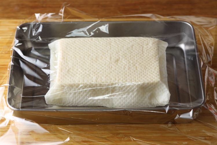 キッチンペーパーをまいた塩豆腐にラップをしている様子
