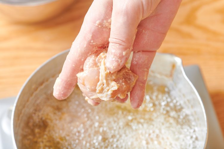 鶏肉を手で丸めながら揚げ油に入れる