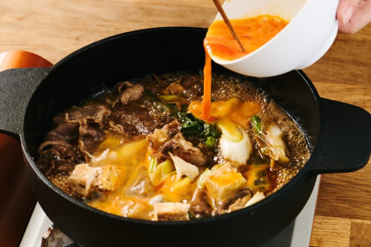 煮込んだすき焼きに溶き卵を流し入れる様子