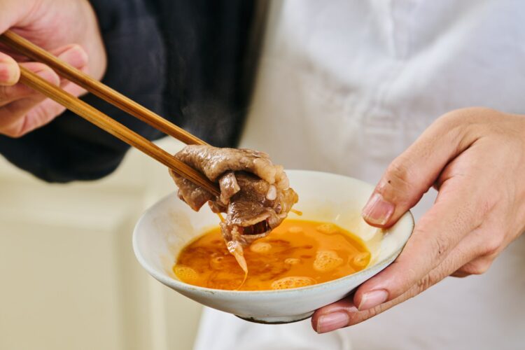加熱した牛肉を溶き卵にくぐらせる様子