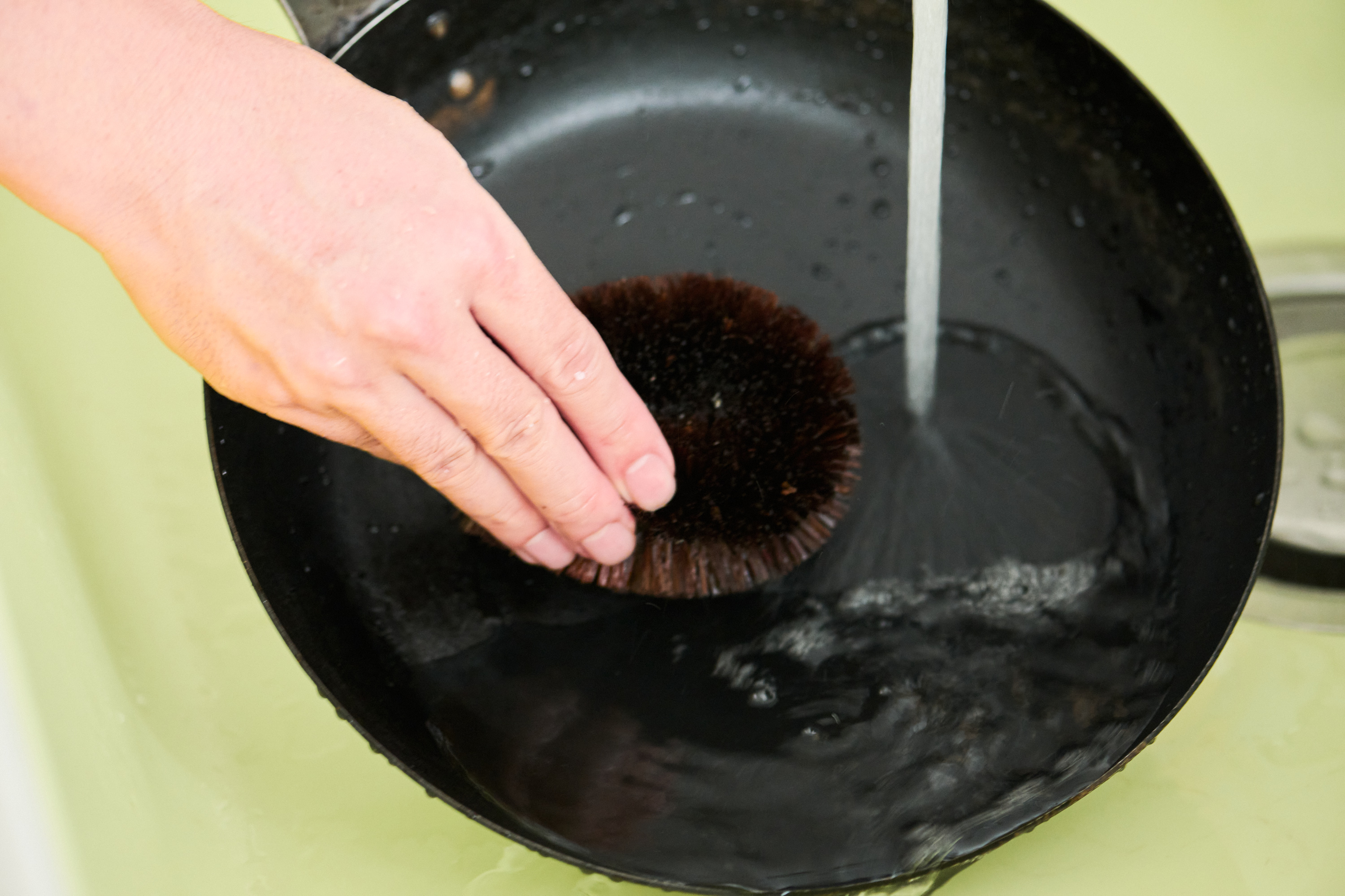 ぬるま湯を流したわしでこすりながら、鉄フライパンの焦げつきを洗い流す