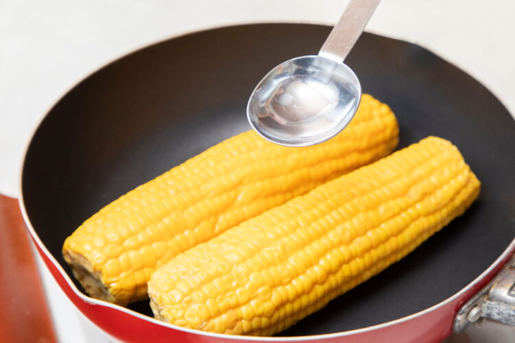 フライパンに入れたトウモロコシに水と塩をふりかける
