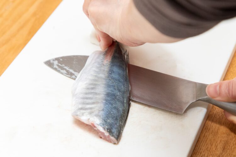 尾をキッチンペーパーで押さえ、アジの尾側から包丁を貫通させる