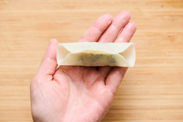 3.皮を二つ折りにし、皮の頂点（上の中心）同士をつまんで、ギュッとしっかり留める